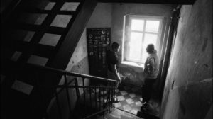 kadr z filmu. klatka schodowa kamienicy, na schodach dwie osoby rozmawiają.