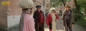 kadr z filmu. dwie kobiety, dwóch mężczyzn na chodniku. kolorowo ubrani, w perukach, boa na szyi, kapeluszach itp.