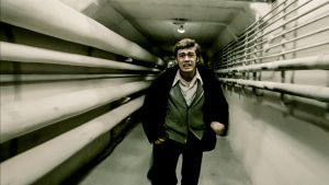mężczyzna, z przerażonym wyrazem twarzy, biegnie przez tunel - wokół niego widać rury